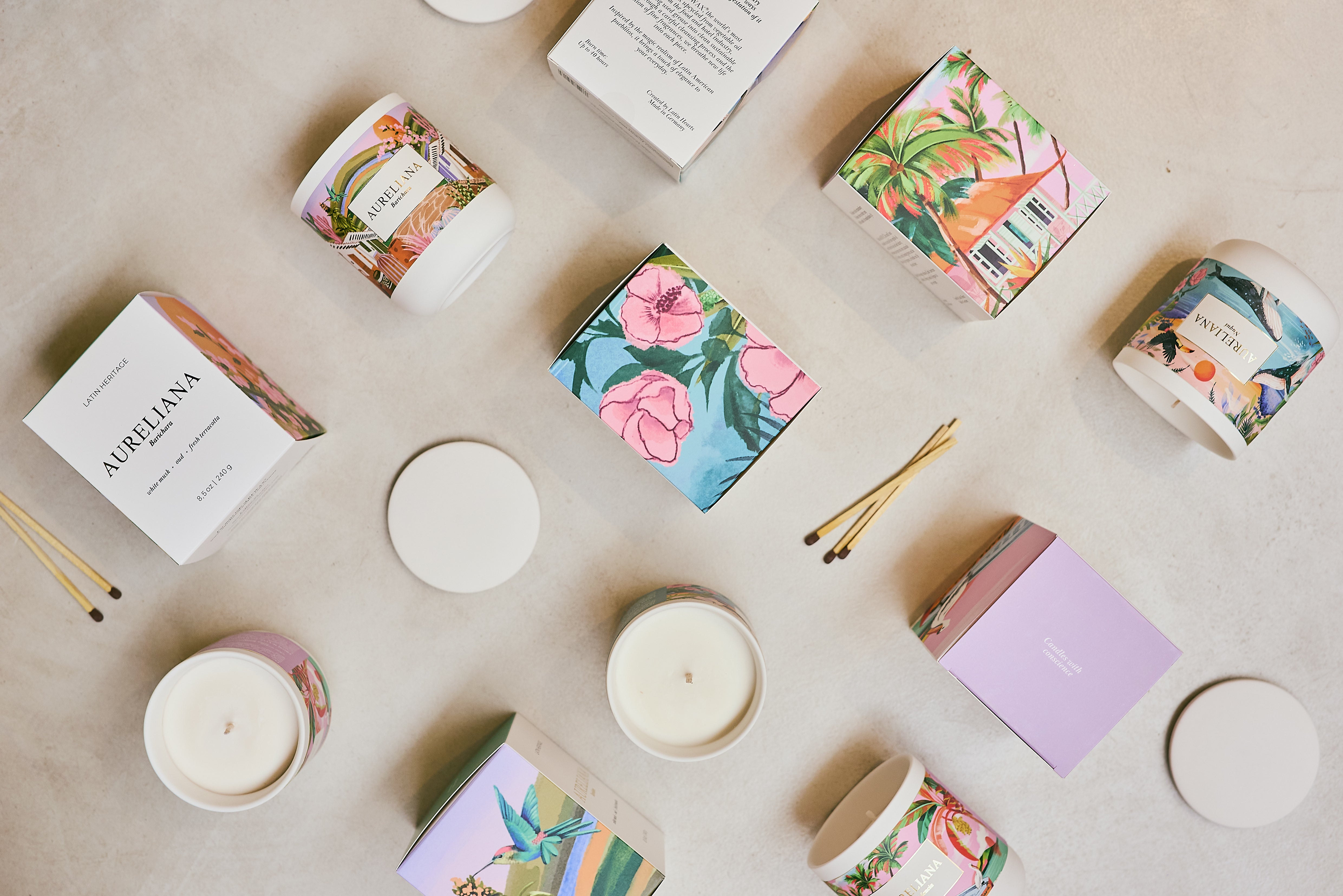 Candles and their packaging with floral designs on a light surface