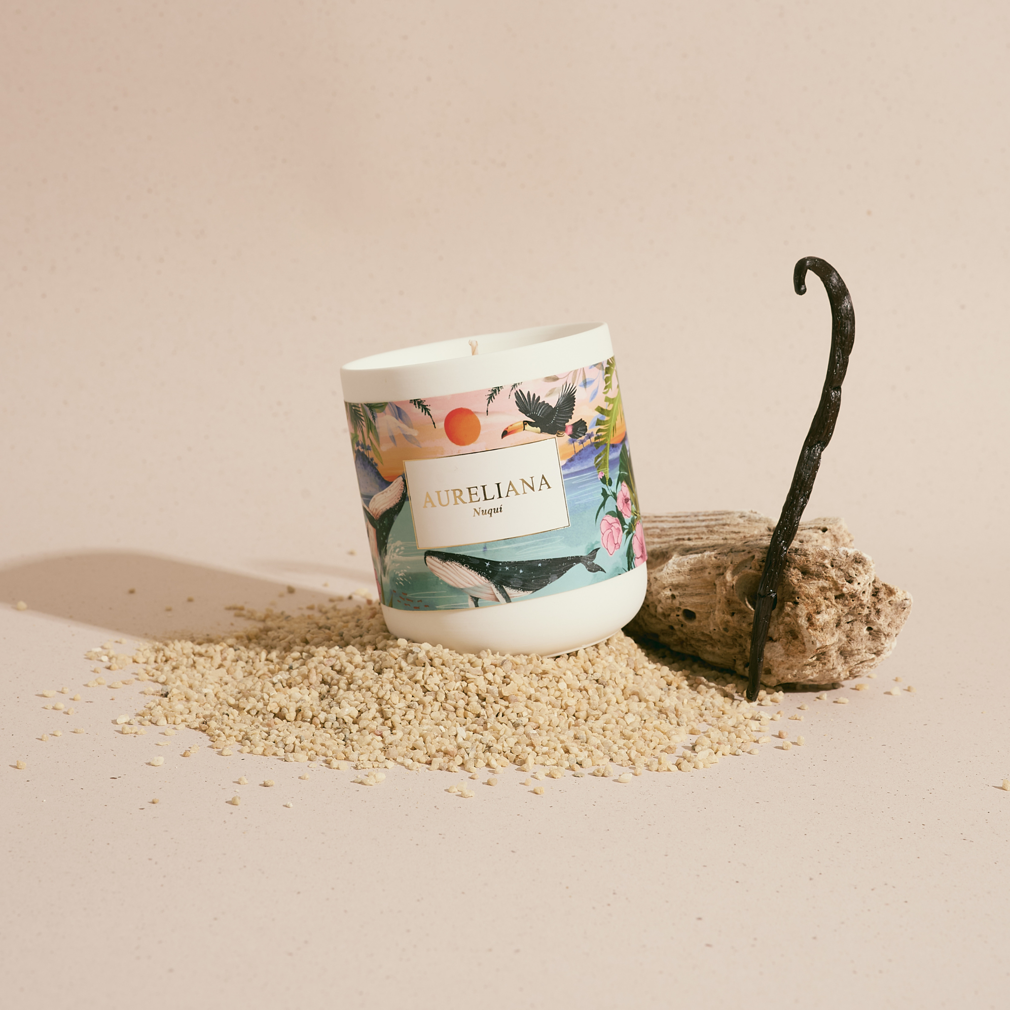 Candle with Aureliana branding on a sandy surface with a vanilla bean.
